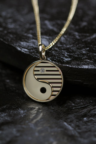 Ying Yang 14K gold pendant necklace over black color rock setting.